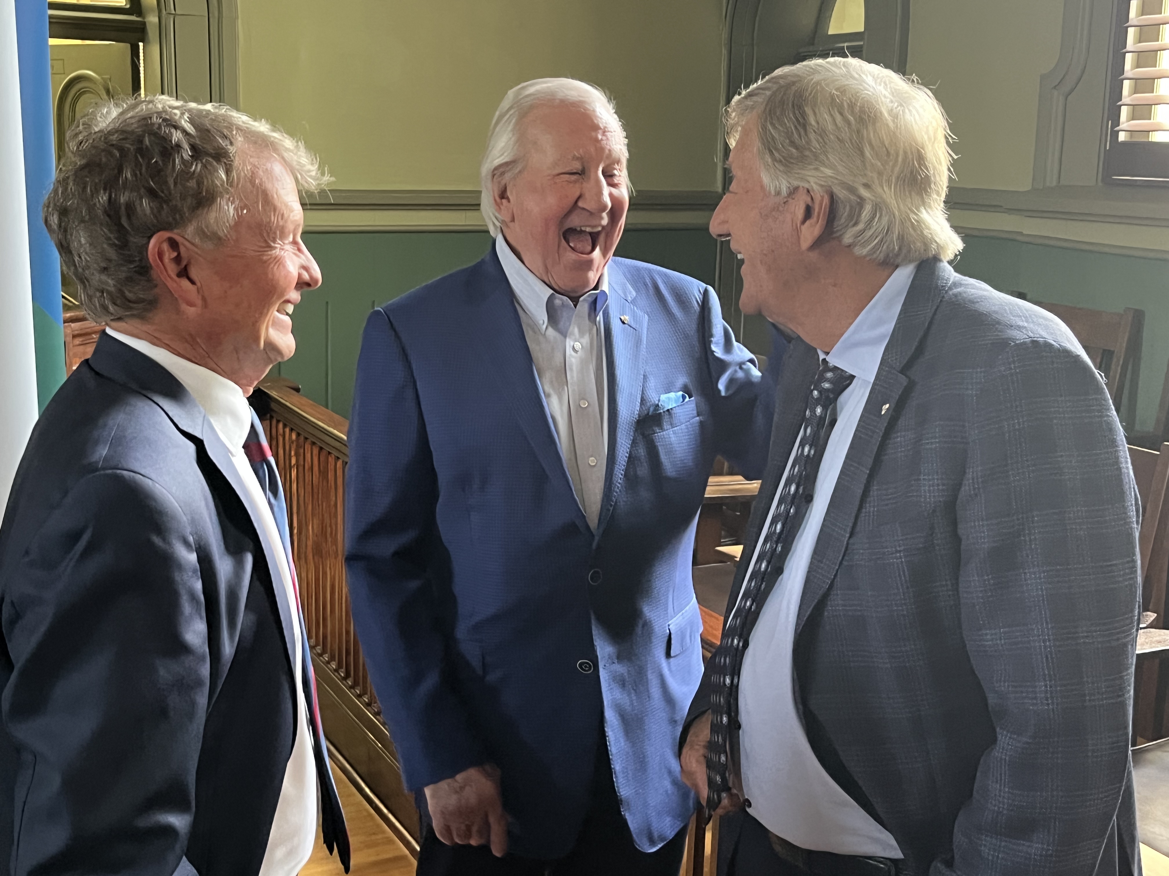three men in suits share a laugh