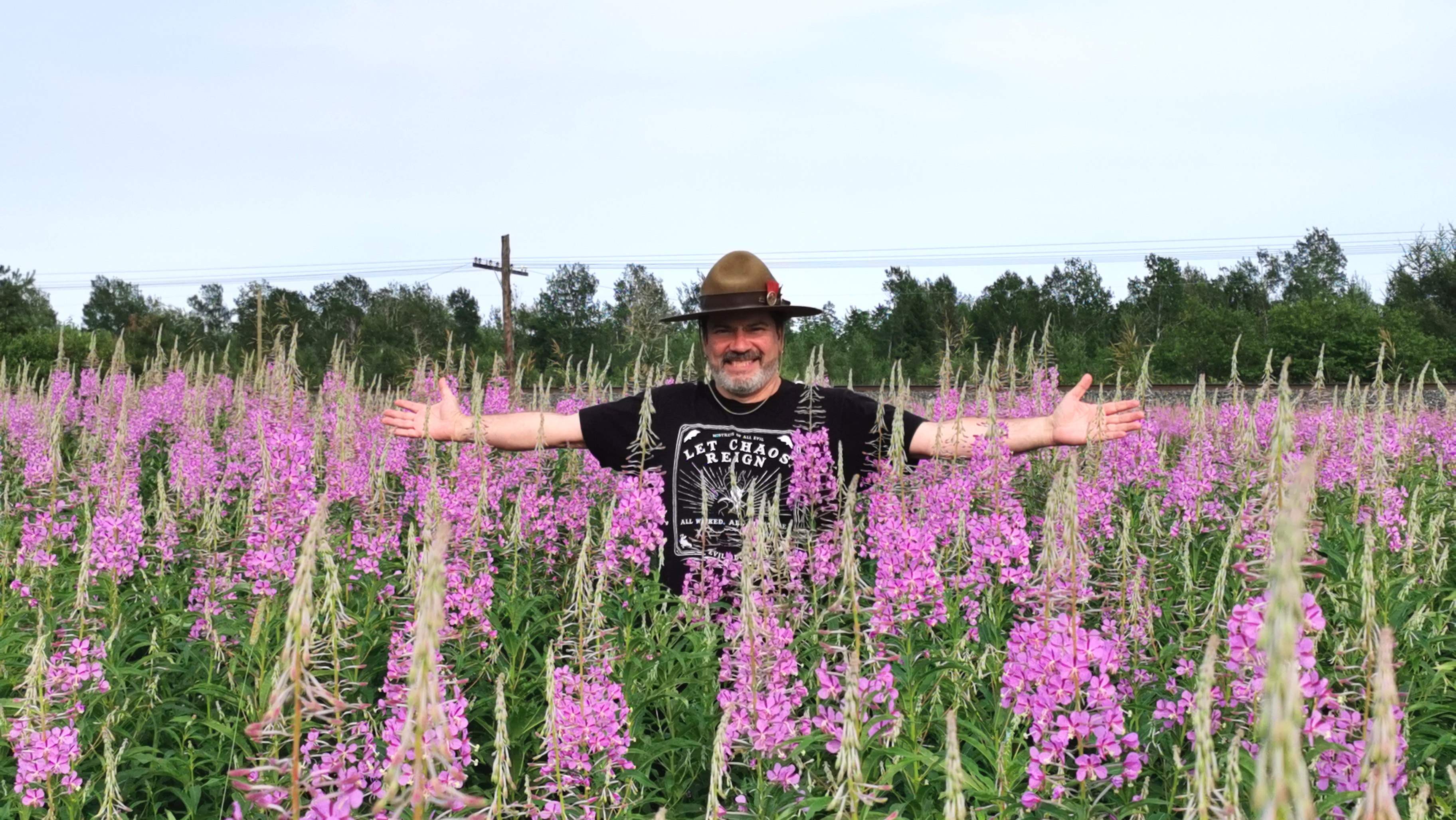 A man with a hat stands in a field of flowers with his arms stretched out