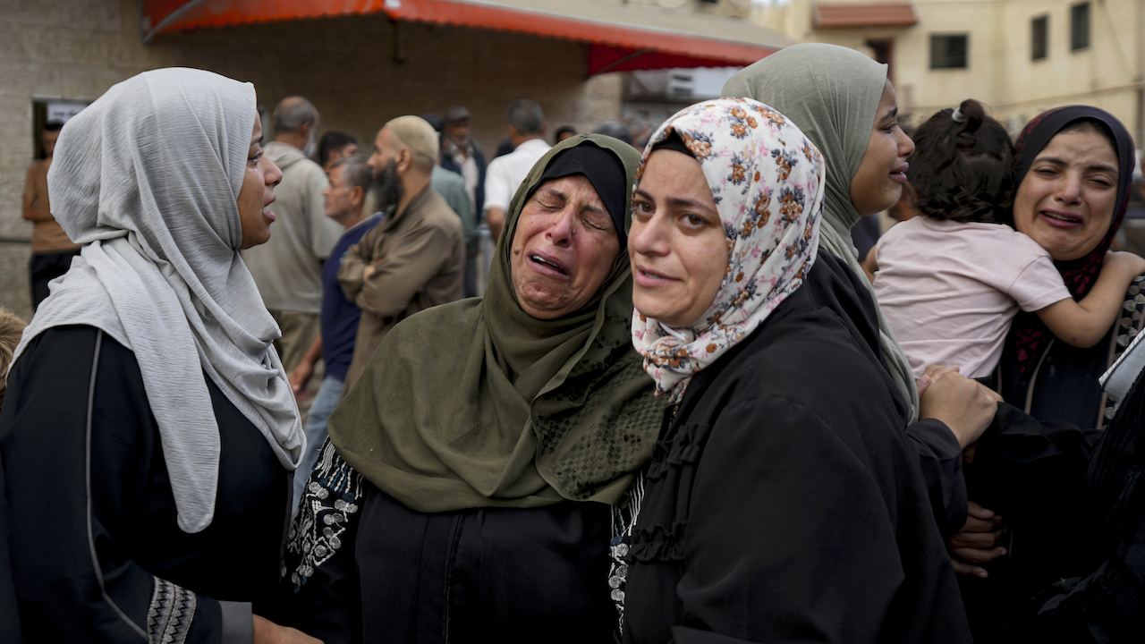 group of morning women in headscarves, one holding a child