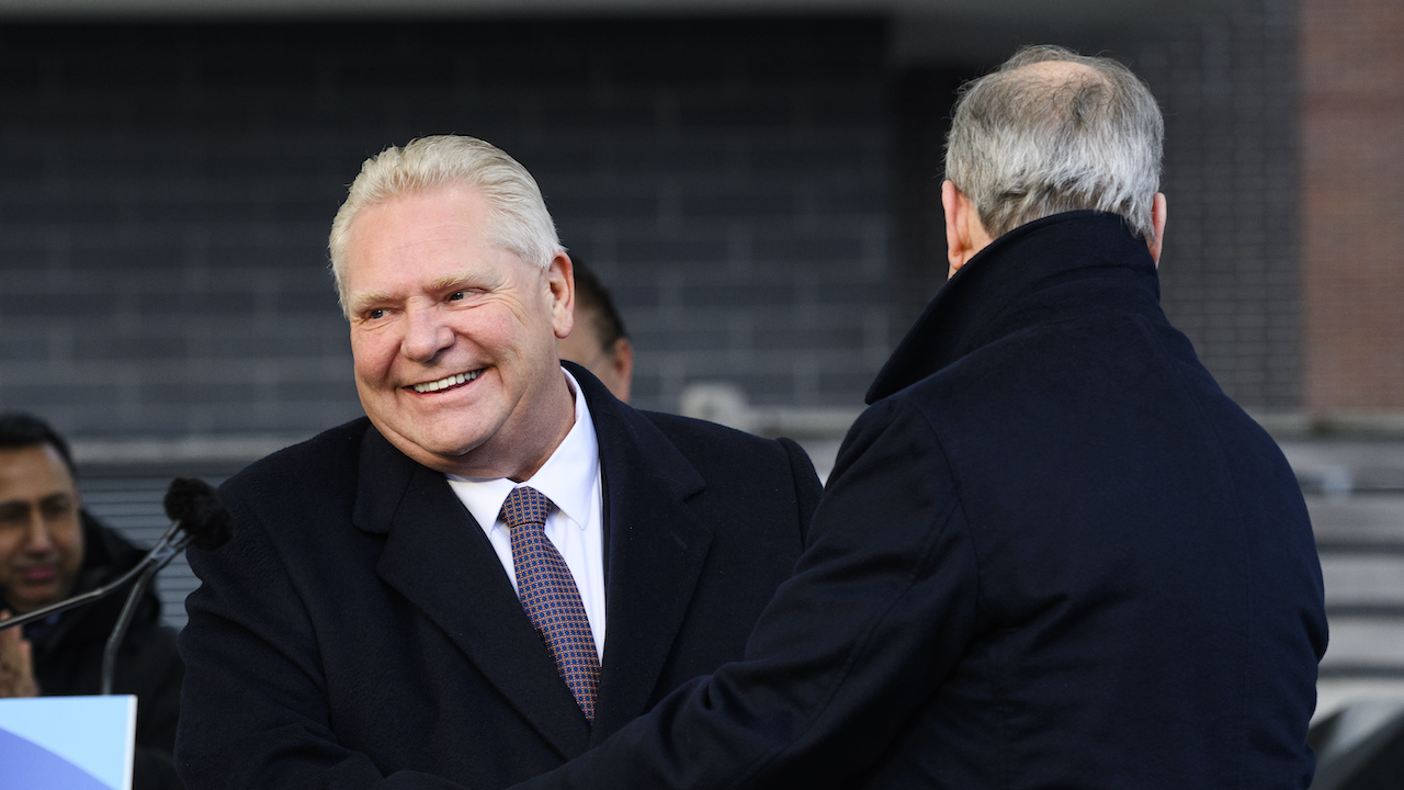suited man laughs next to man in dark coat with his back turned