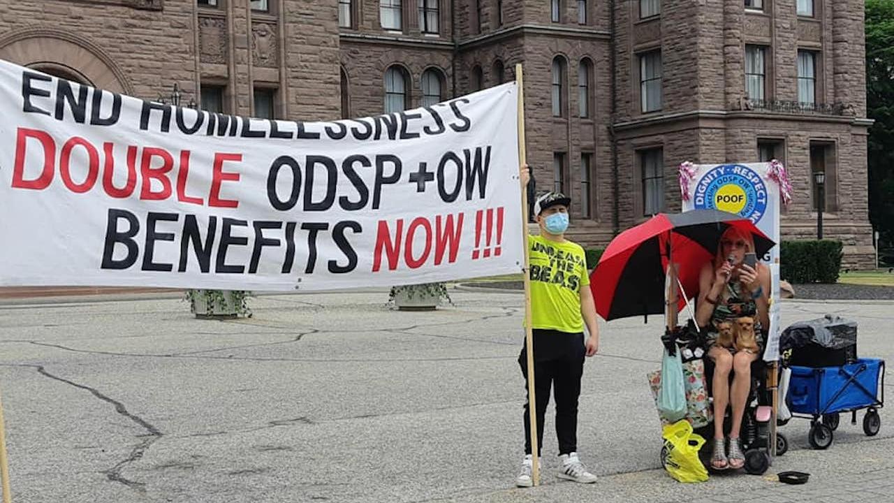 masked man and woman in wheelchair next a banner reading "End homelessness — double ODSP and OW benefits now!"